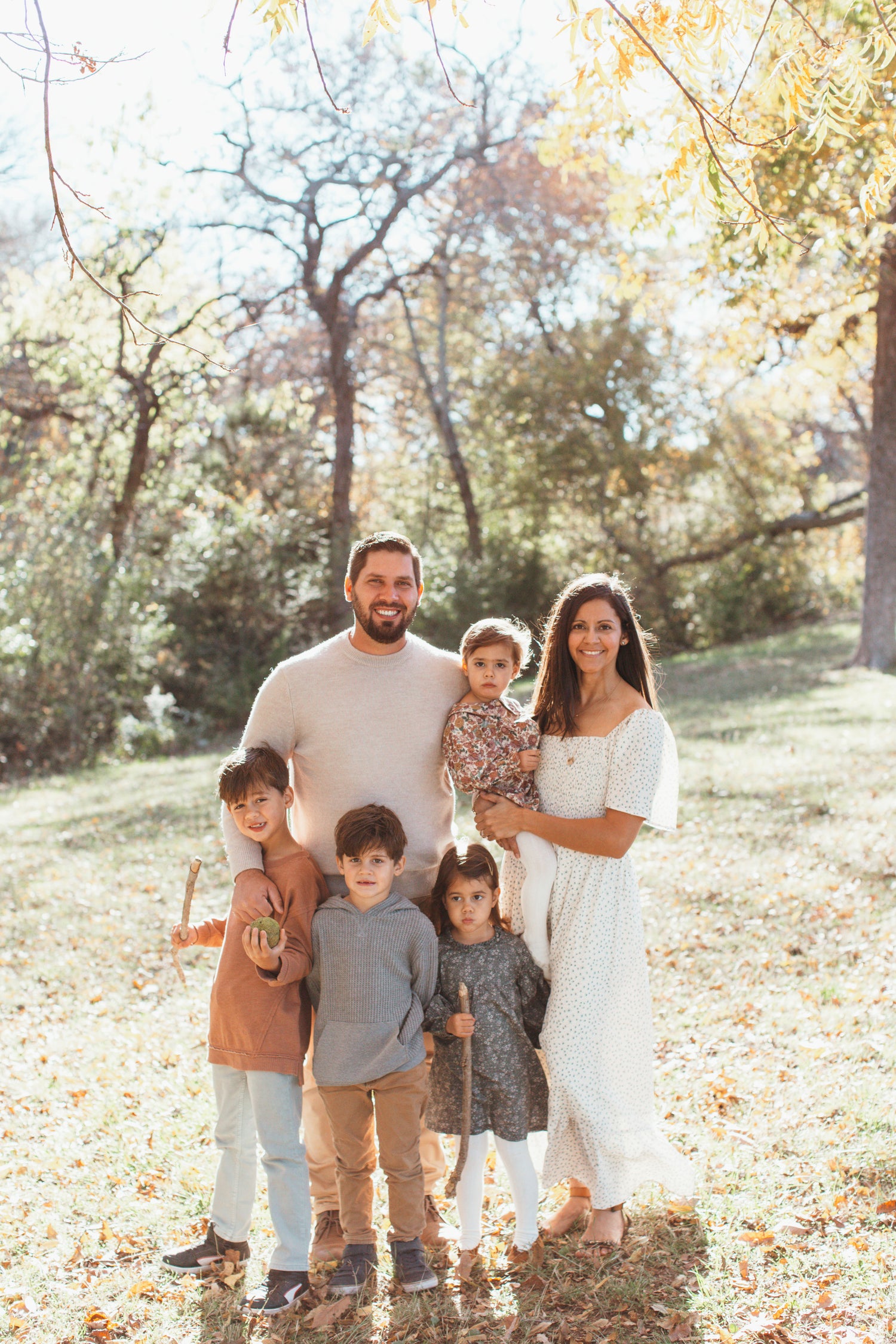 Family of six standing outdoors in a park with trees and grass.