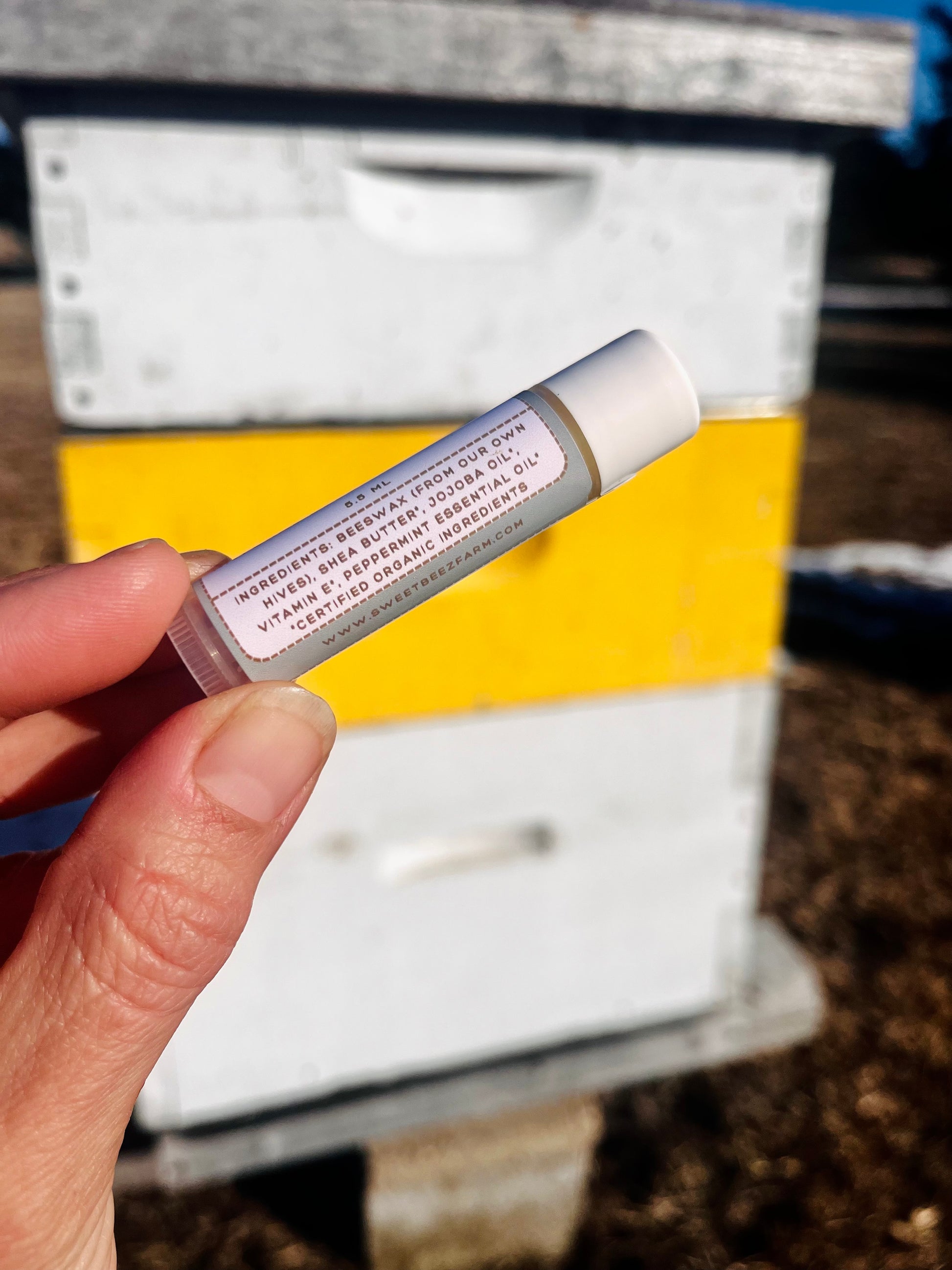 Hand holding a small cylindrical object with text in front of a beehive.