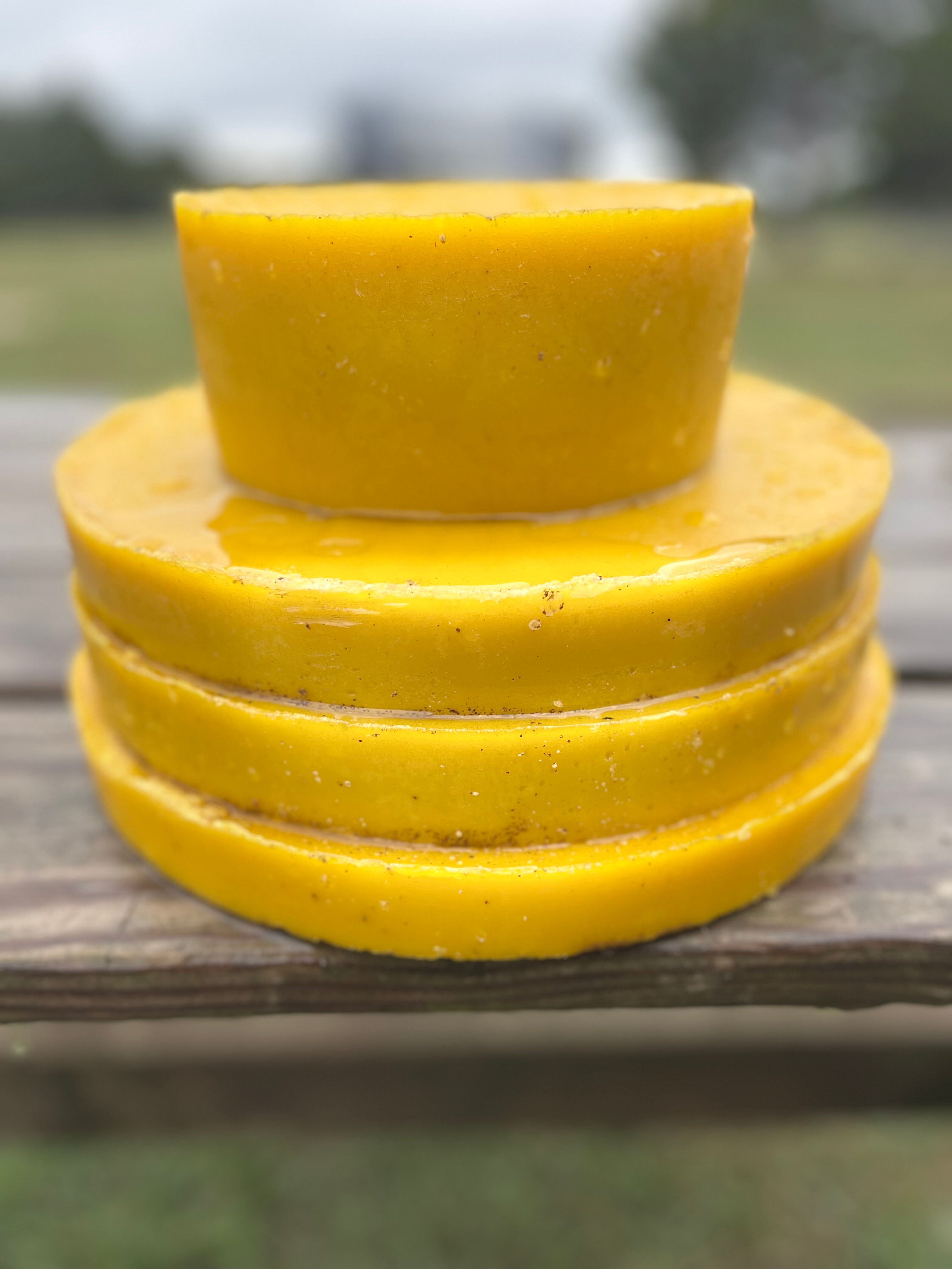 Stack of yellow beeswax blocks on a wooden surface with a blurred natural background