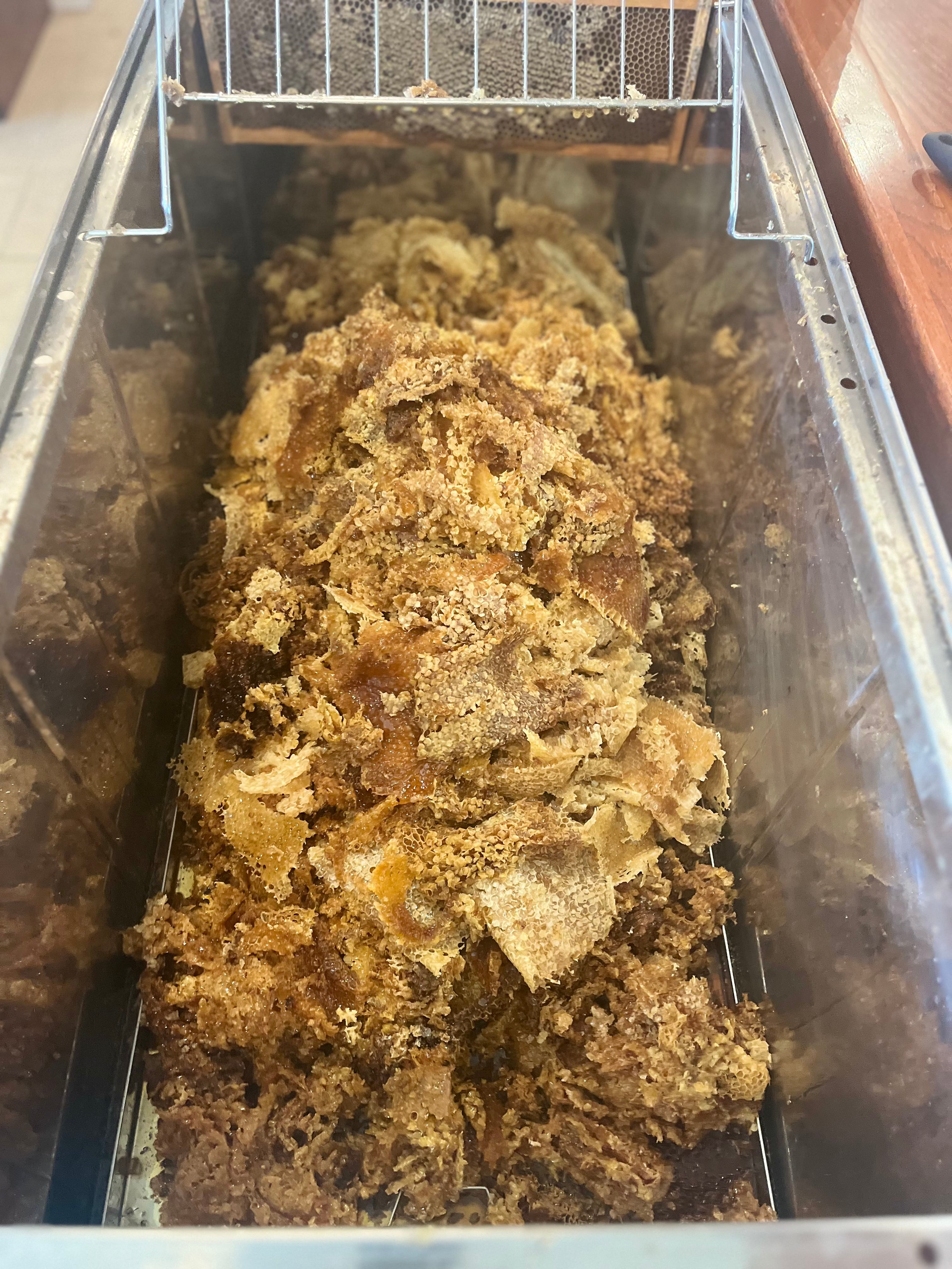 Raw unprocessed beeswax in a container with a metal rack above it